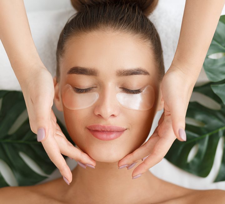 Woman with eye patches having face massage at beauty salon